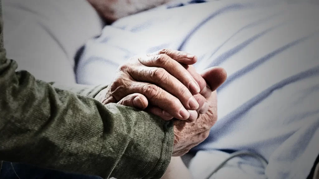 Äldre kvinna håller sin döende mans hand i närbild