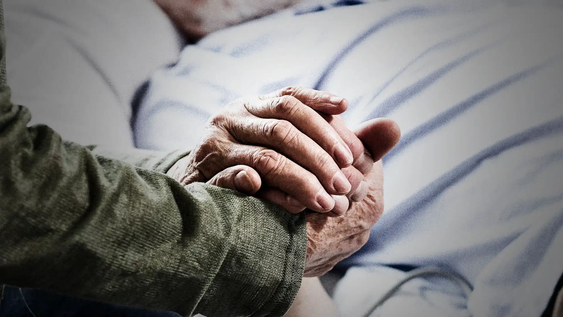 Äldre kvinna håller sin döende mans hand i närbild