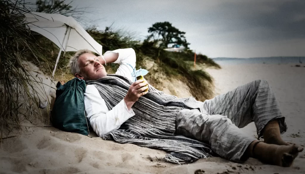Fattig person ligger på en strand och dricker en paraplydrink