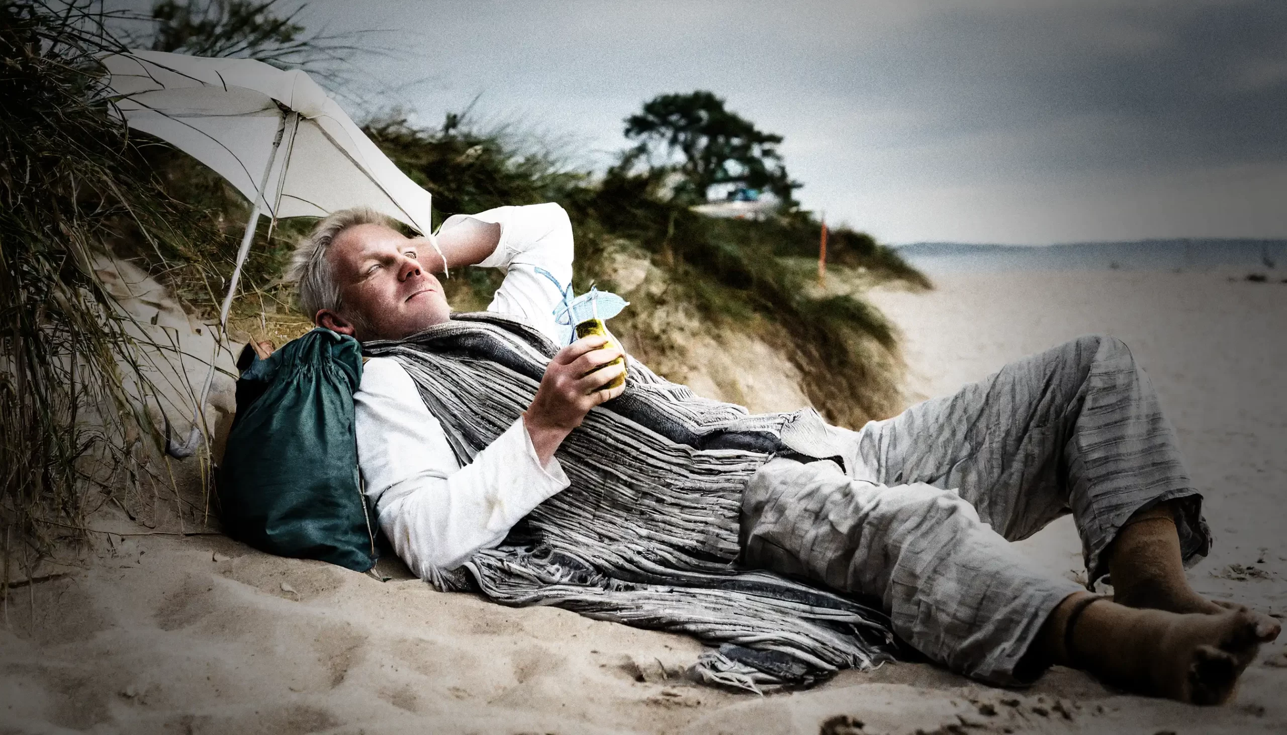 Fattig person ligger på en strand och dricker en paraplydrink