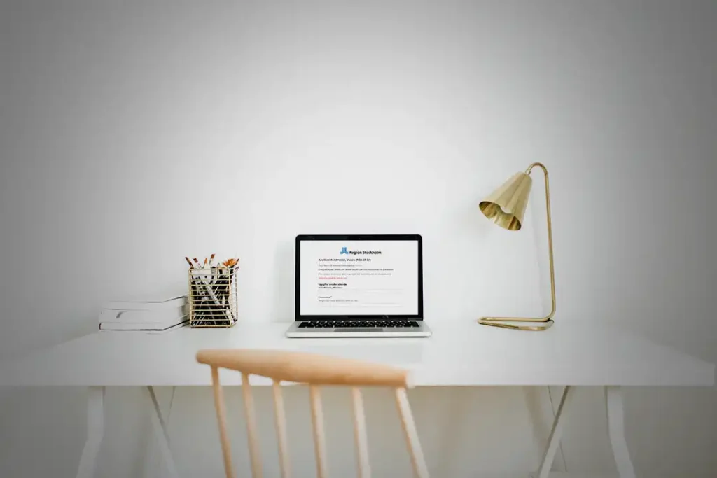 En laptop står på ett skrivbord med en lampa i guldfärg.