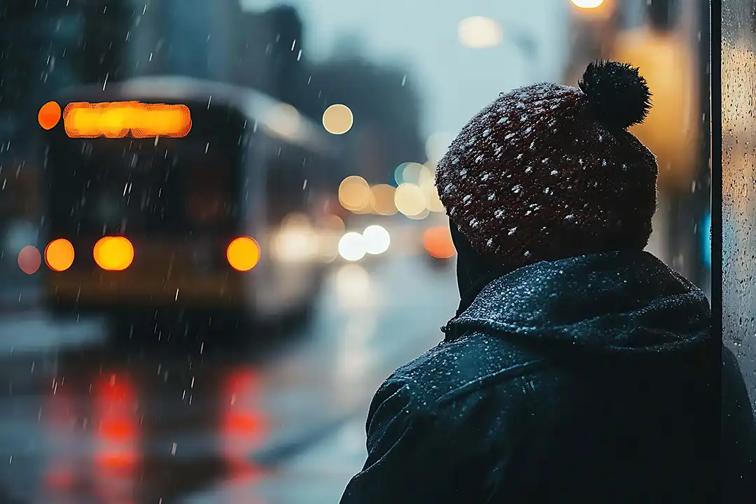 Kvinna sitter ensam vid en busshållplats, det snöar och är kallt