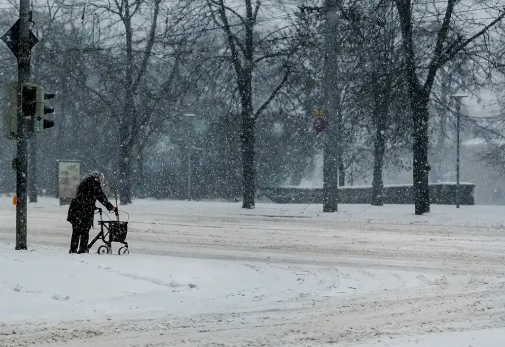 Äldre kvinna går med rollator över en oplogad väg