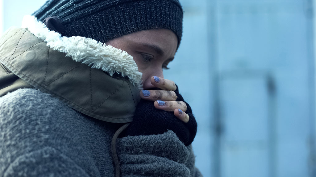 Kvinna står i kylan värmer sina händer, tonen är blå