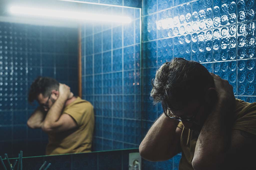En man står i badrummet man ser honom från sidan i en spegel